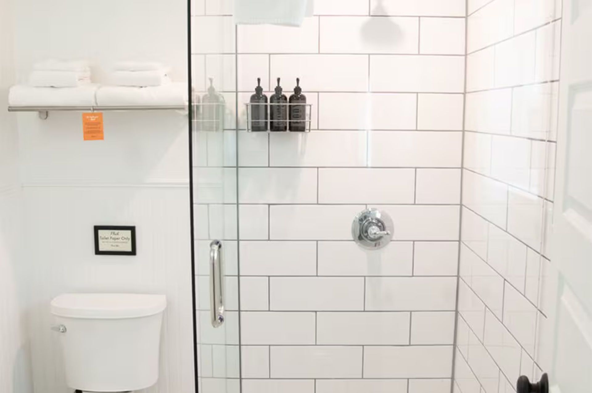 White bathroom with shower, toilet, and towels. The shower has white subway tile.