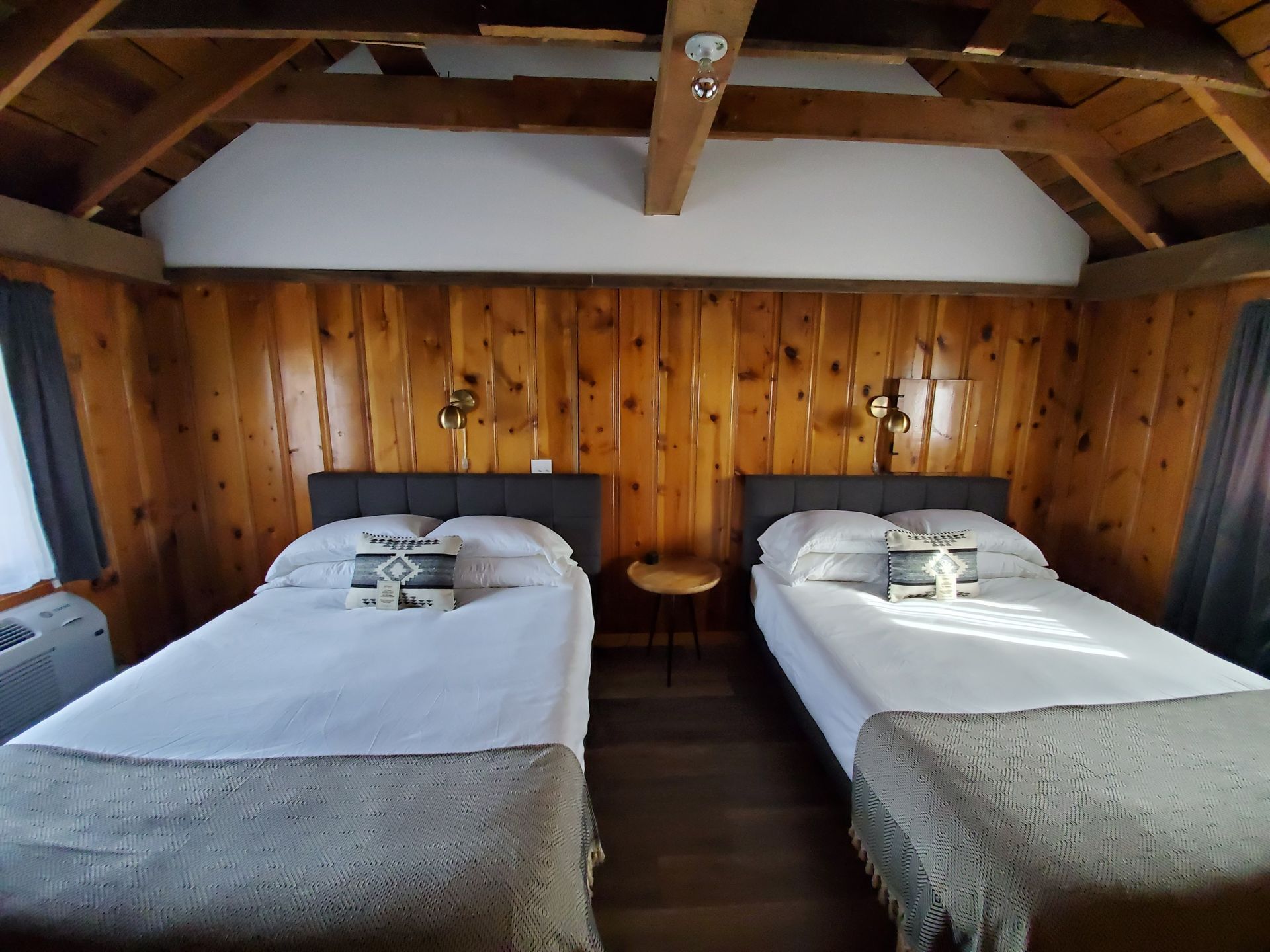 Two twin beds in a room with wood paneling. Small table between beds. Beige and white bedding.