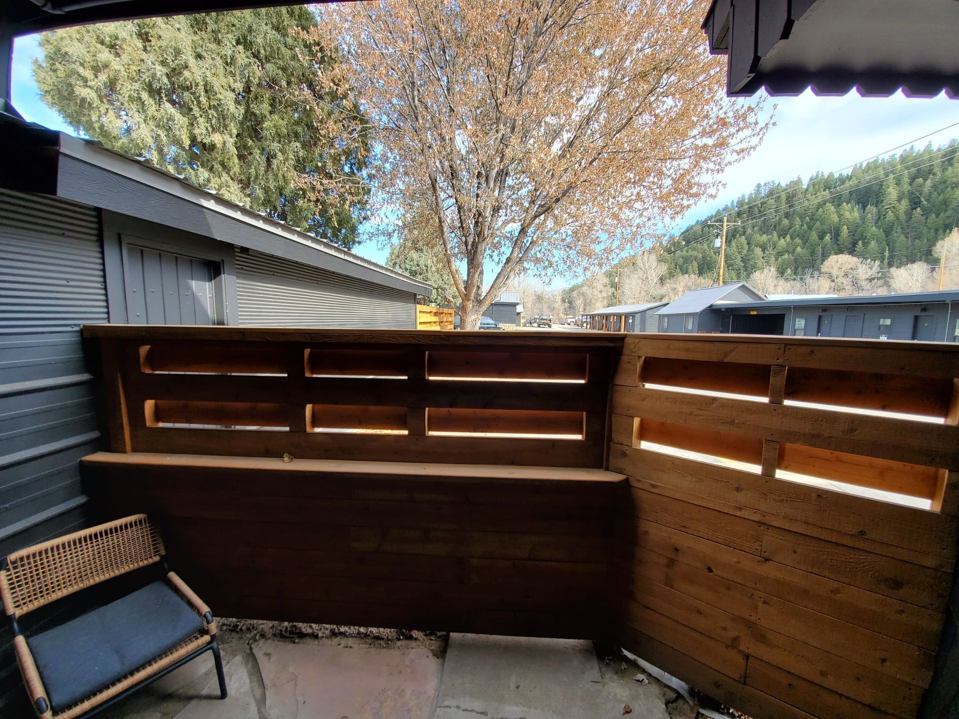 Cozy outdoor patio with wooden walls and seating. A tree is visible beyond the wall.