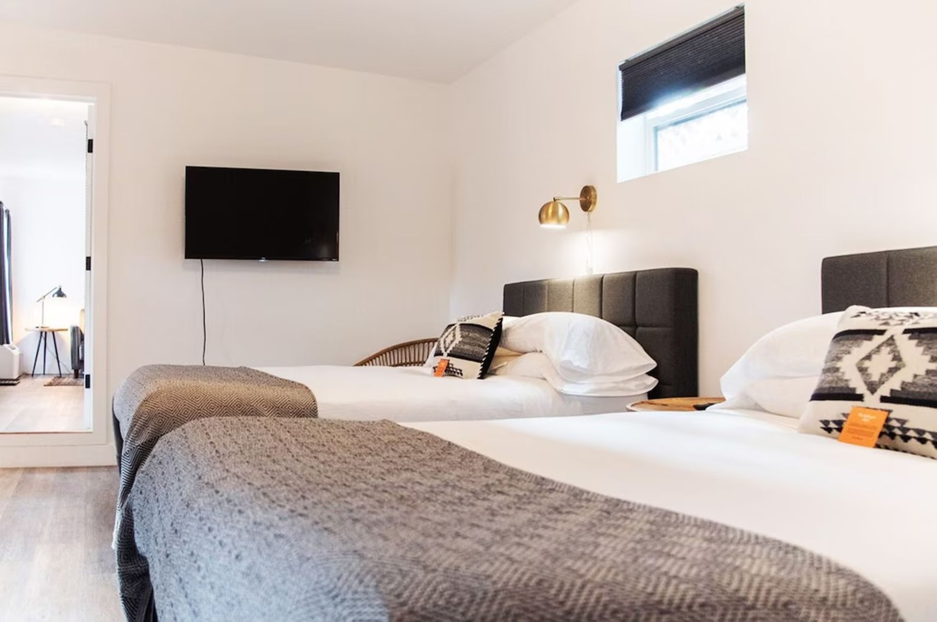 Bedroom with two beds, white walls, TV, doorway to another room.