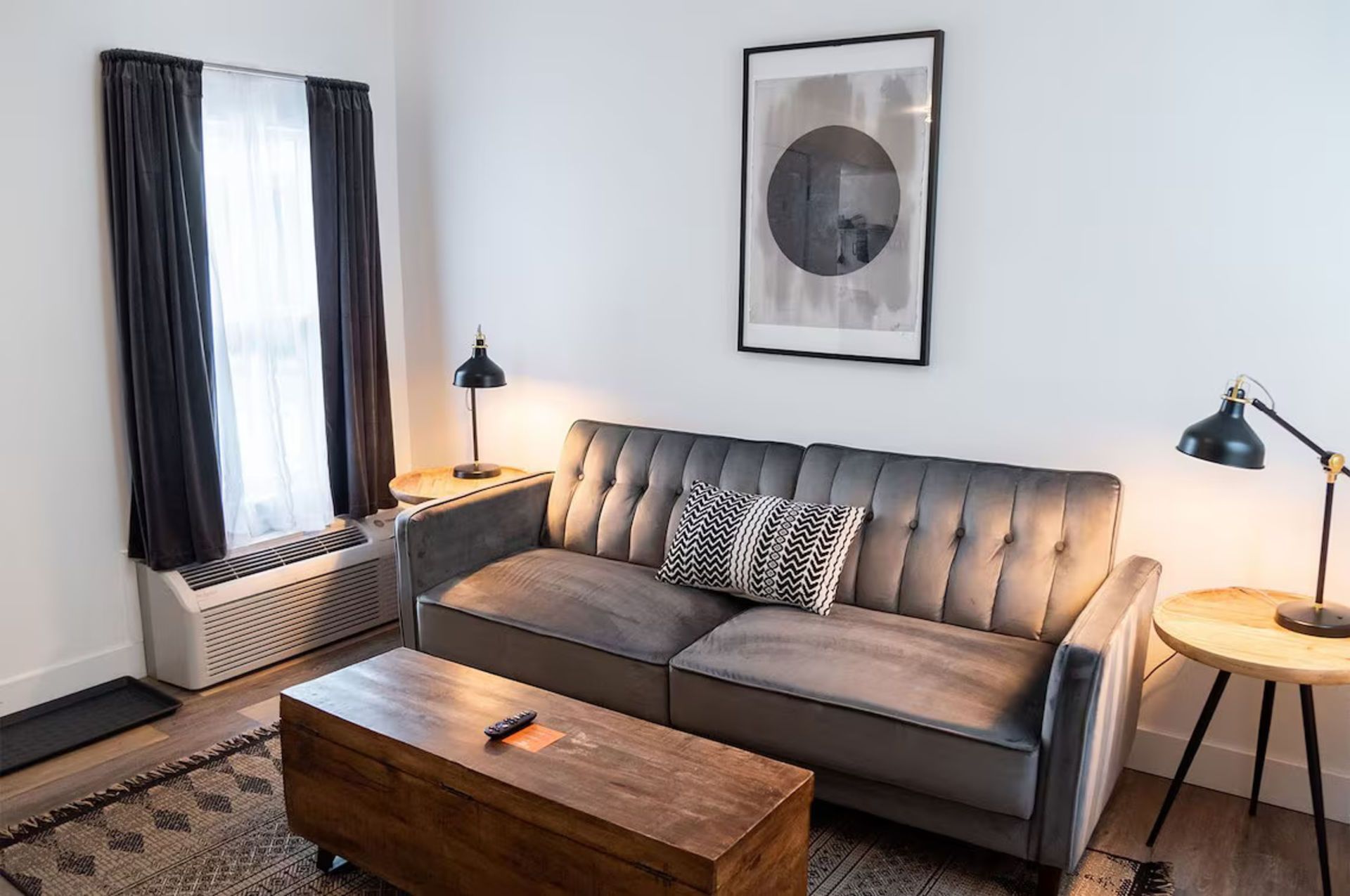Cozy living room with gray sofa, wooden coffee table, side tables, window, and framed artwork.