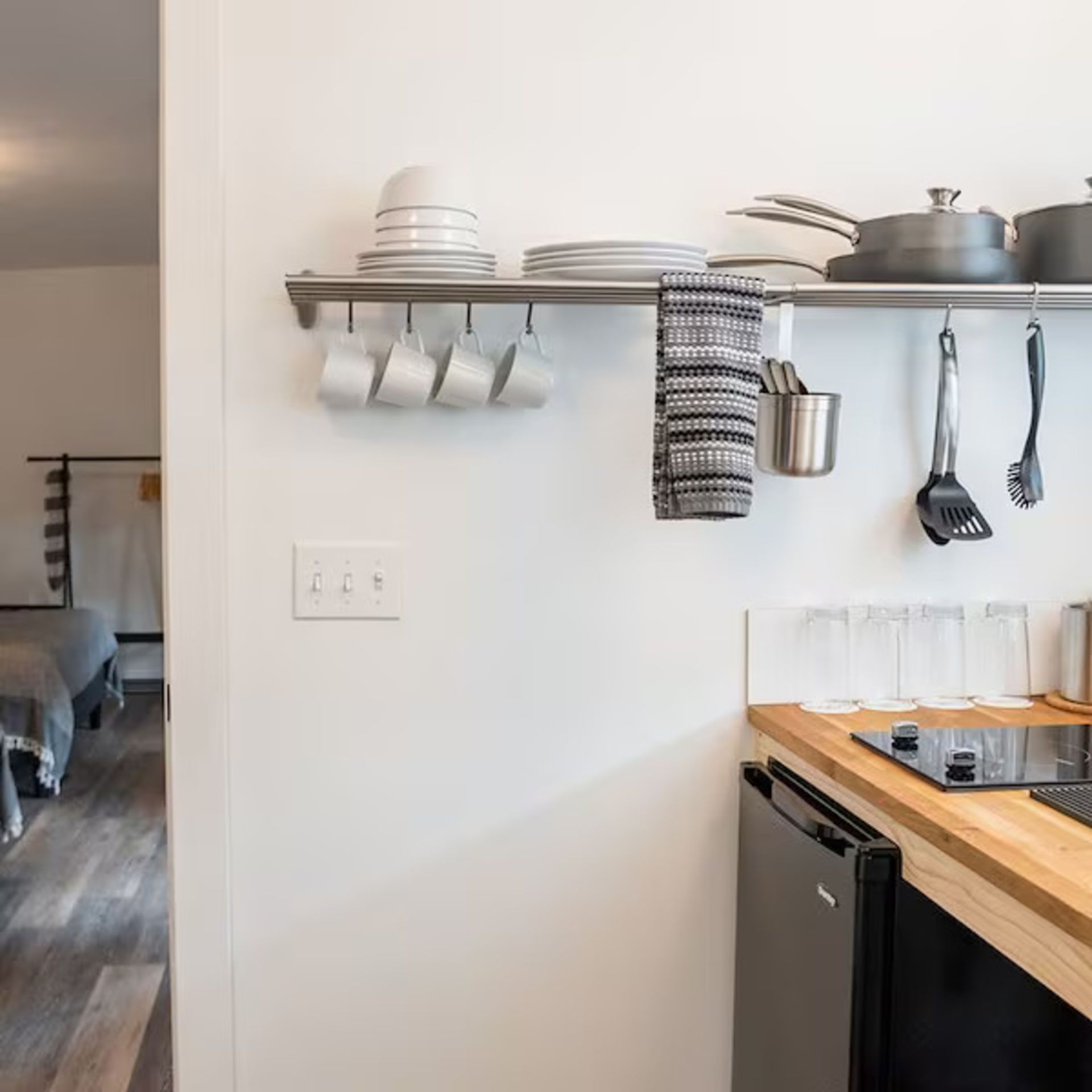 Small kitchen with stainless steel shelf holding dishes, cups, and cooking utensils.