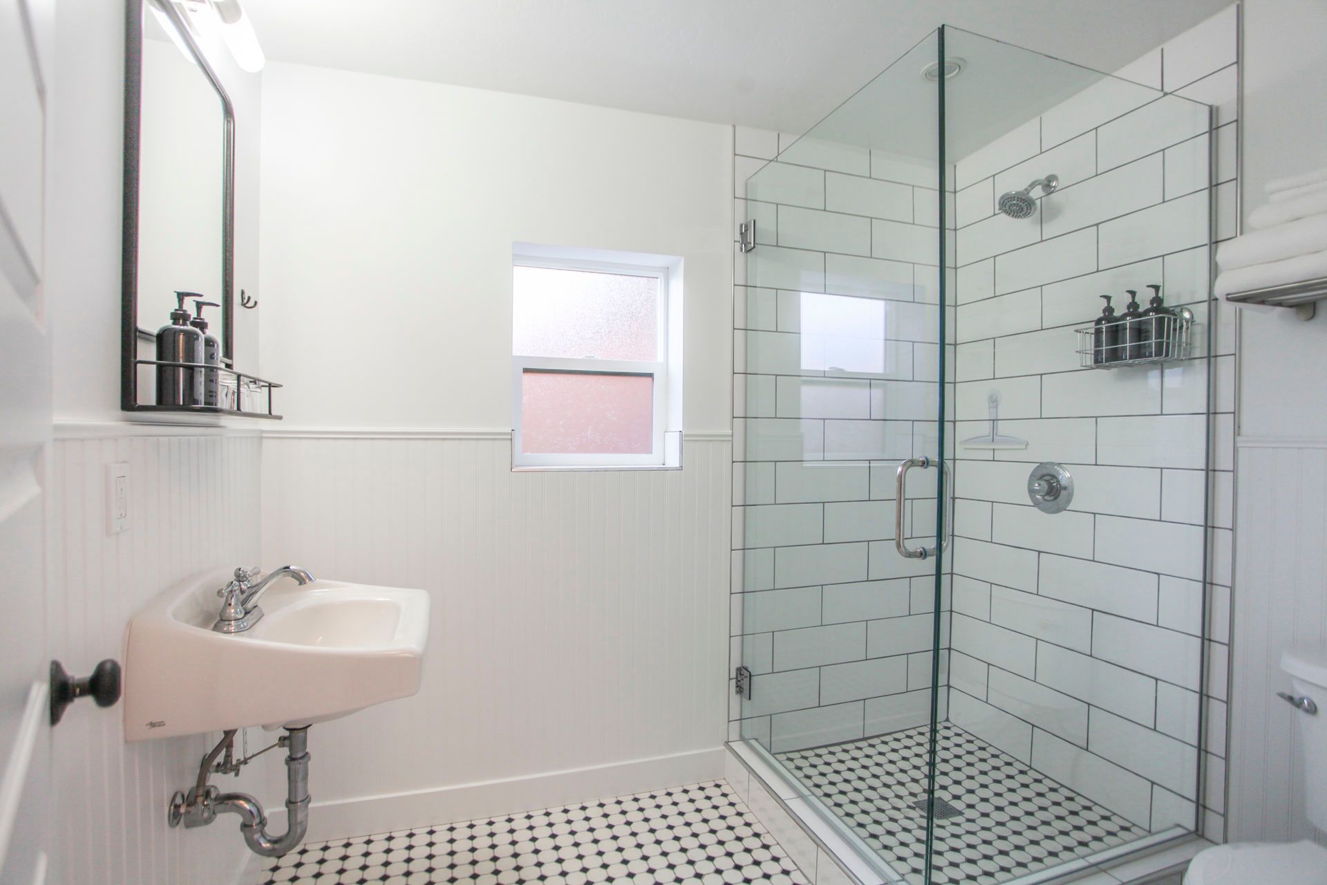 White bathroom with a glass shower, pink sink, and black and white tiled floor.