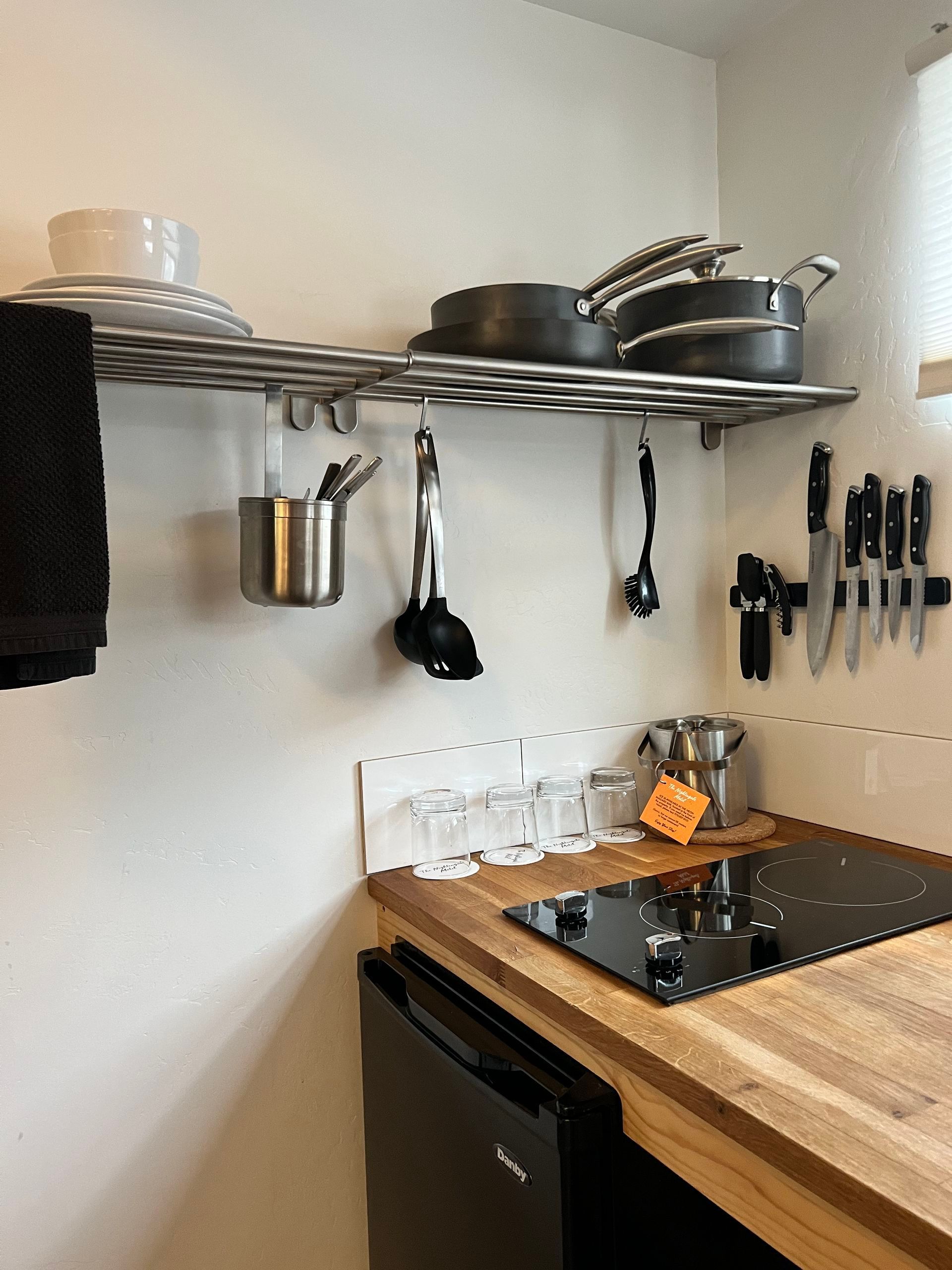 Small kitchen with stainless steel shelving holding pots, pans, and utensils, over a stovetop.