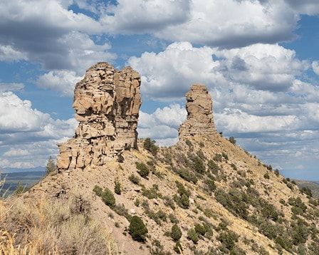 Two weathered rock formations atop a hillside, under a cloudy blue sky.
