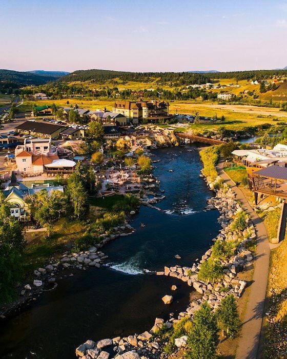 Townscape with river flowing through, rocky waterfalls, buildings, and greenery under a blue sky.