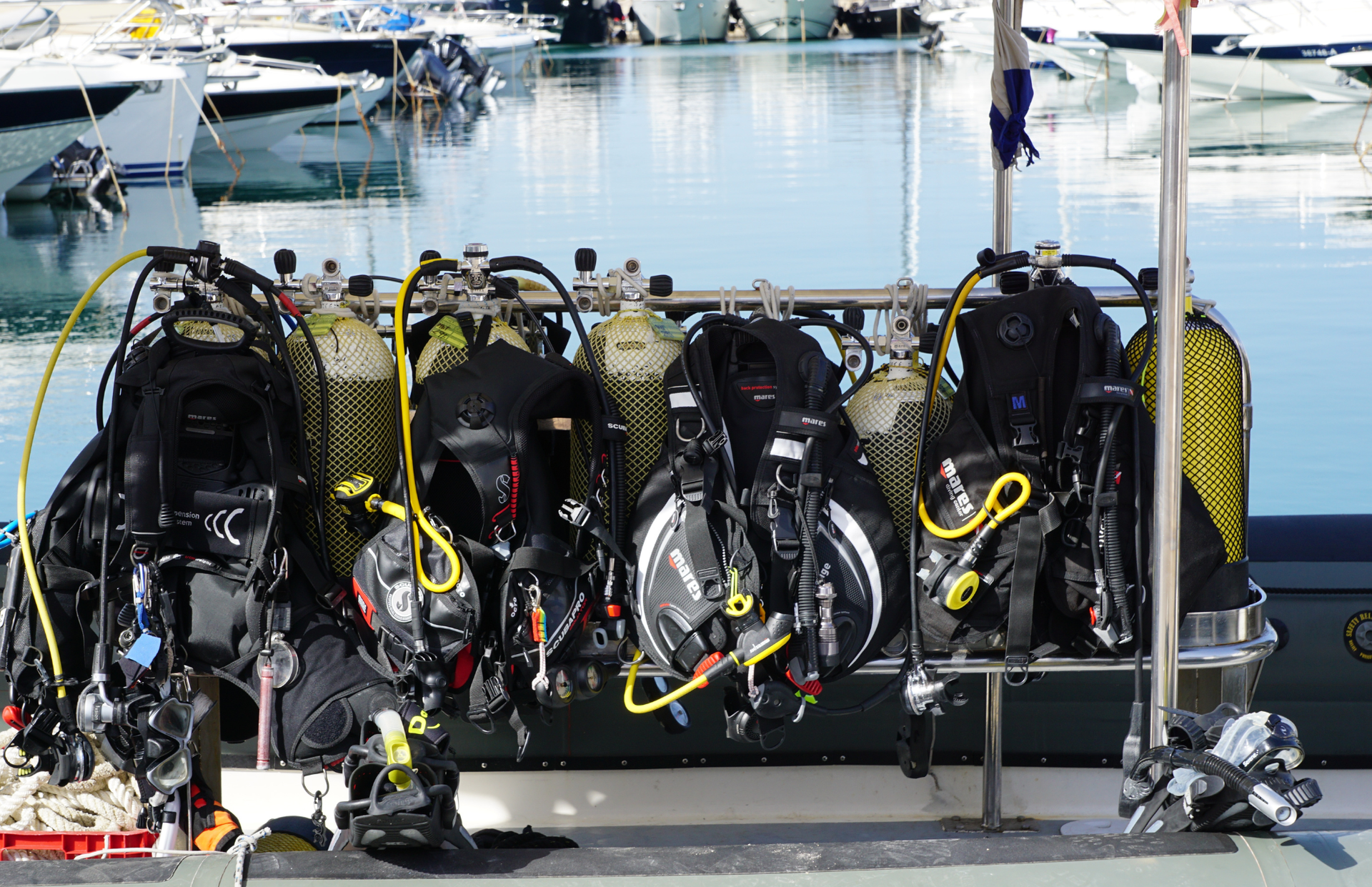 Four scuba diving tanks and regulators on a dock with boats in the marina behind them