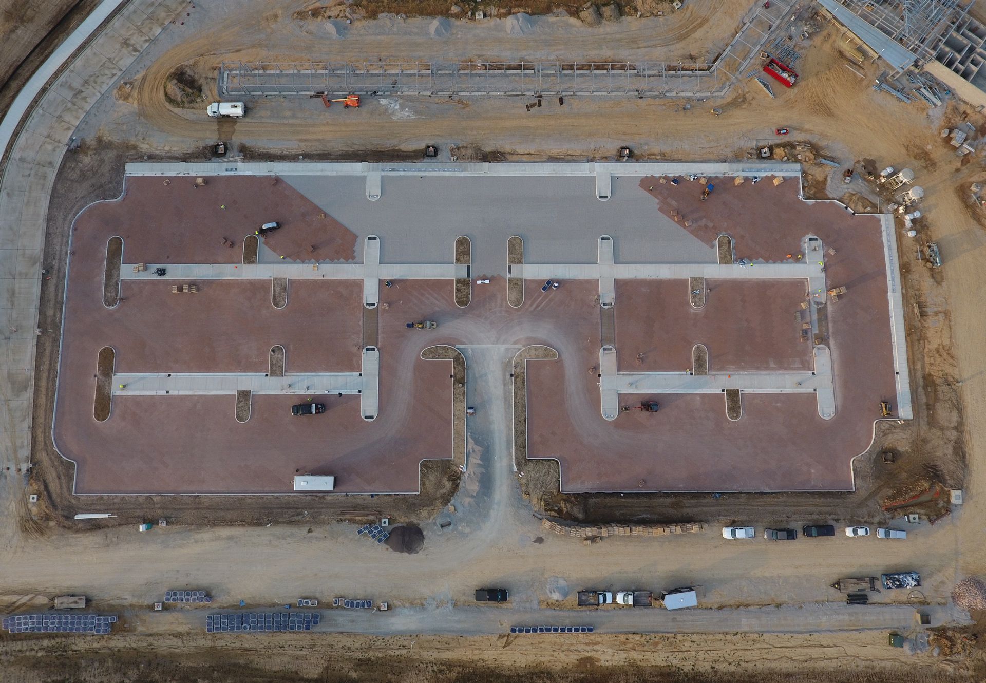 Aerial view of a large paver parking lot under construction on a dirt site with surrounding roads.