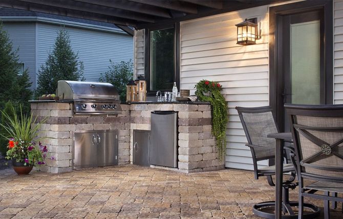 Covered patio with stainless steel grill, stone counter, and outdoor dining chairs beside a house