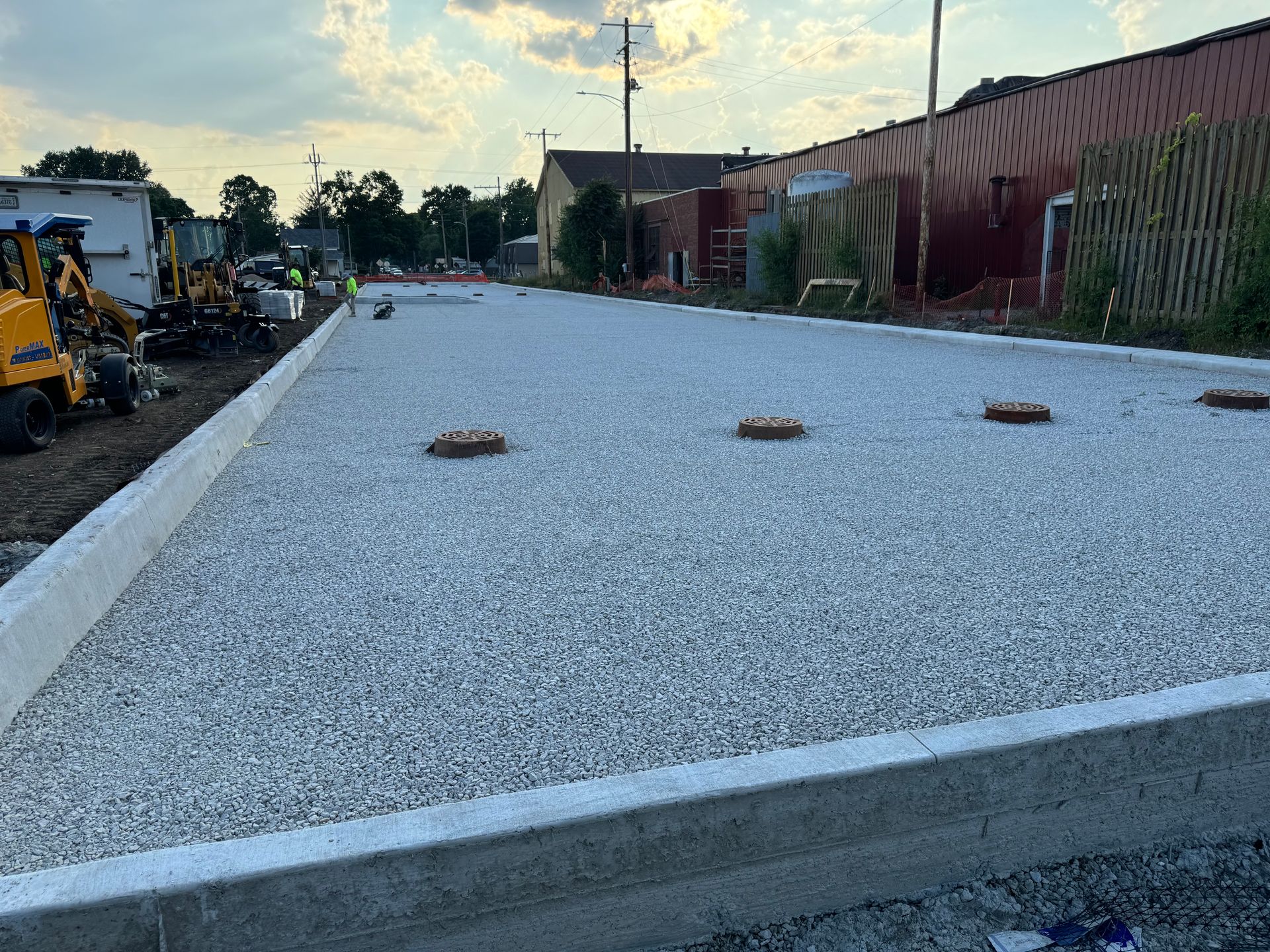 Gravel-filled construction site with concrete edging and equipment along the sides at sunset