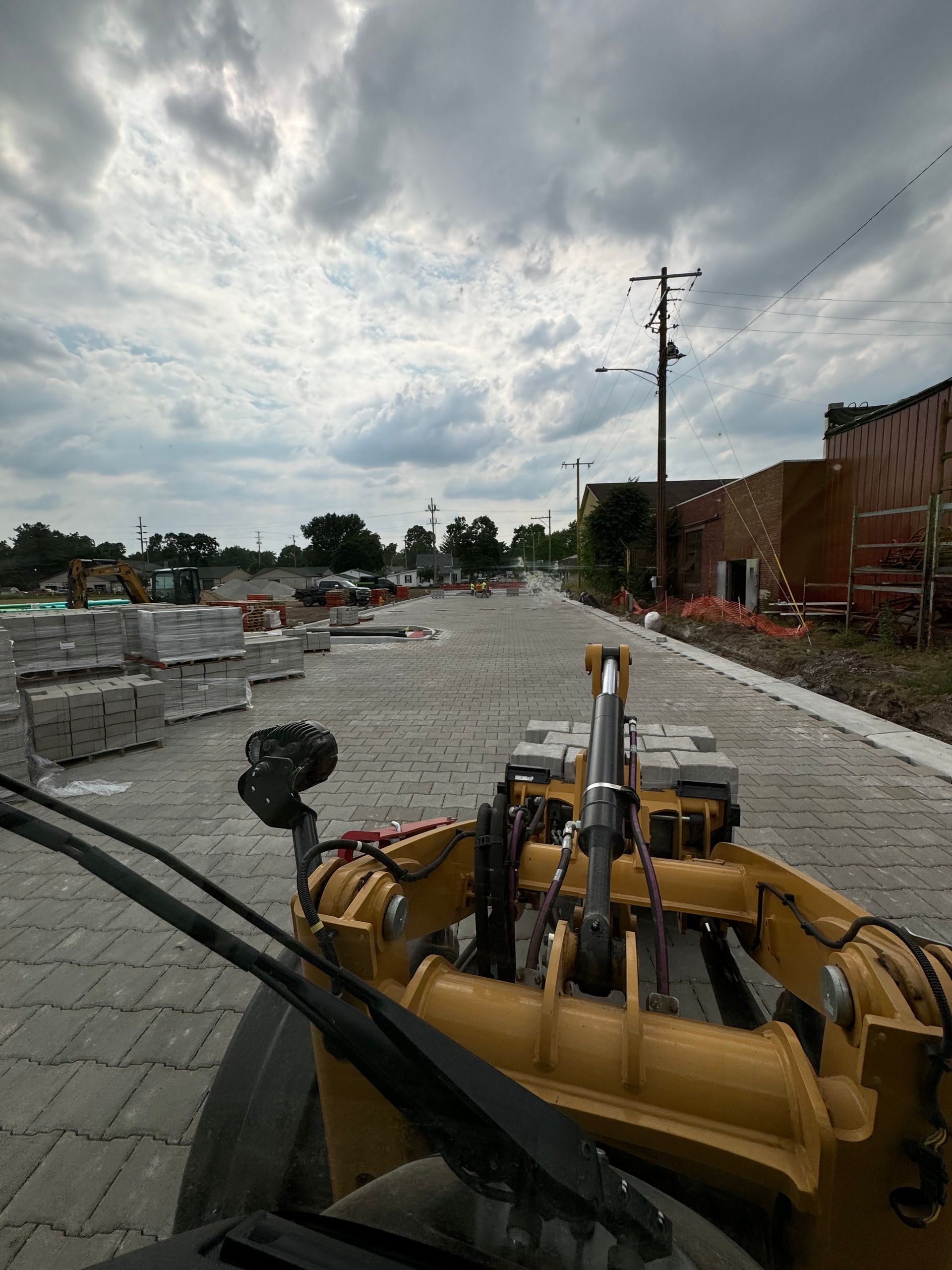 Yellow machinery on a flooded street under a cloudy sky, with floodwater blocking the road