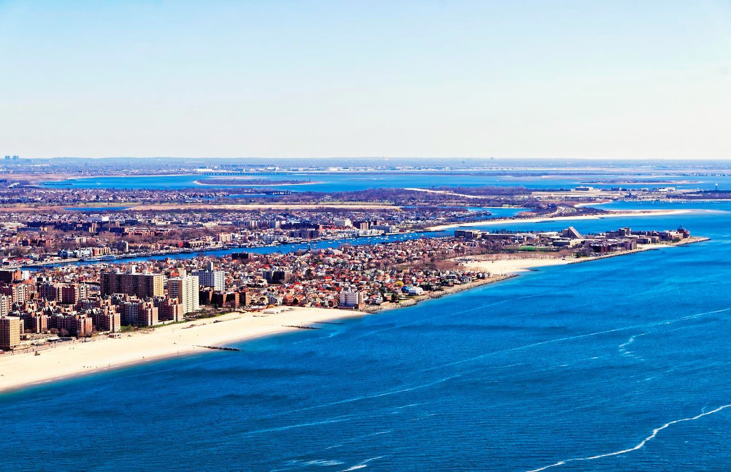 Aerial view of a coastal city with sandy beach, dense buildings, and bright blue ocean