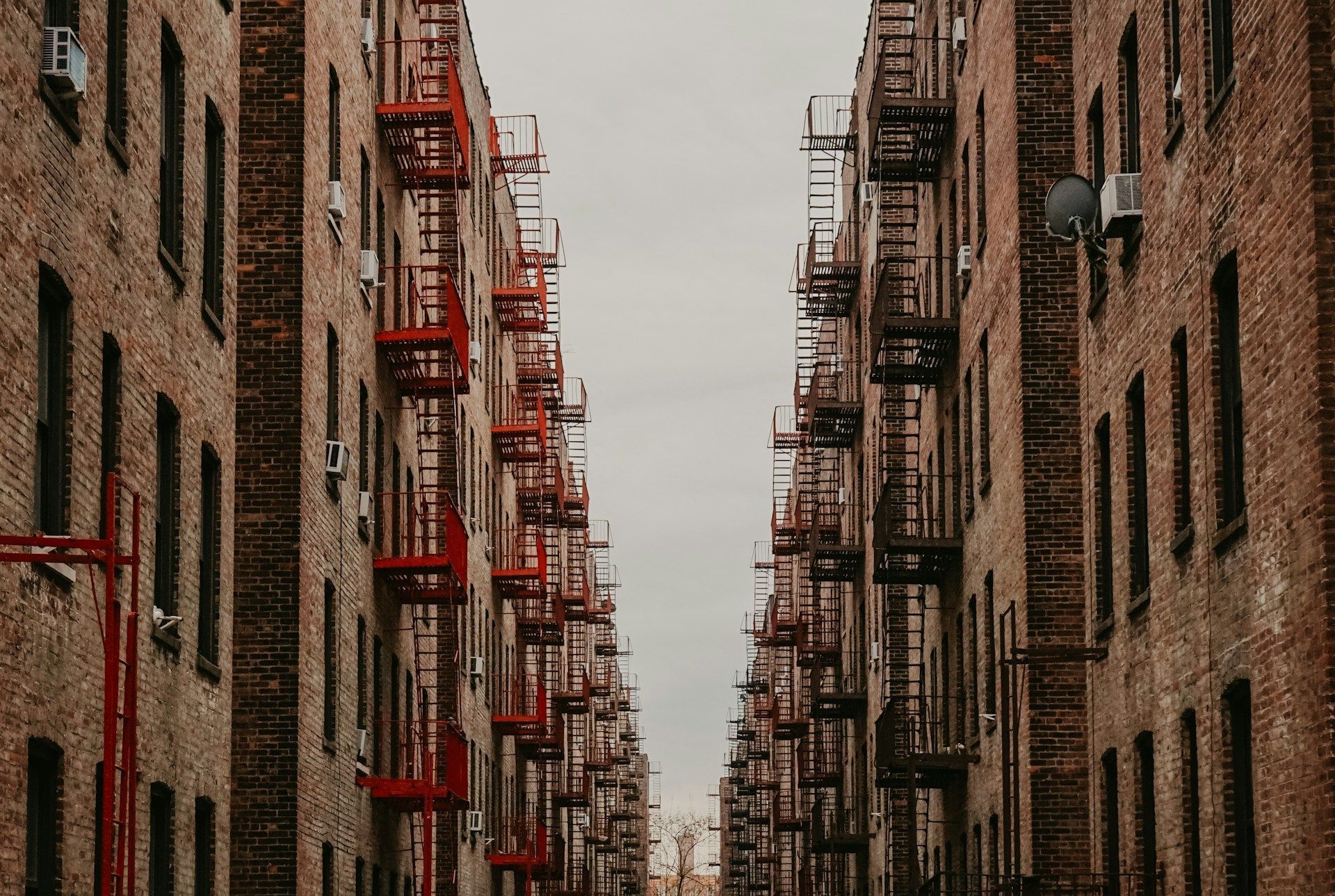 Narrow brick apartment alley with red fire escapes on both sides