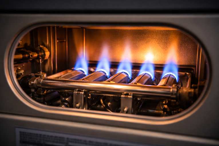 Inside of a furnace, five blue flames burn brightly from gas burners.