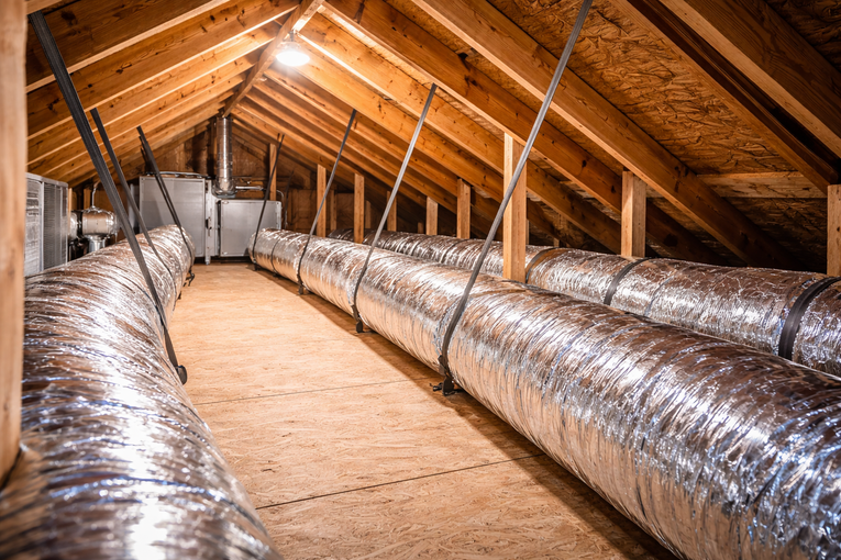 Attic with ductwork and a central air unit, wooden beams, and insulation.