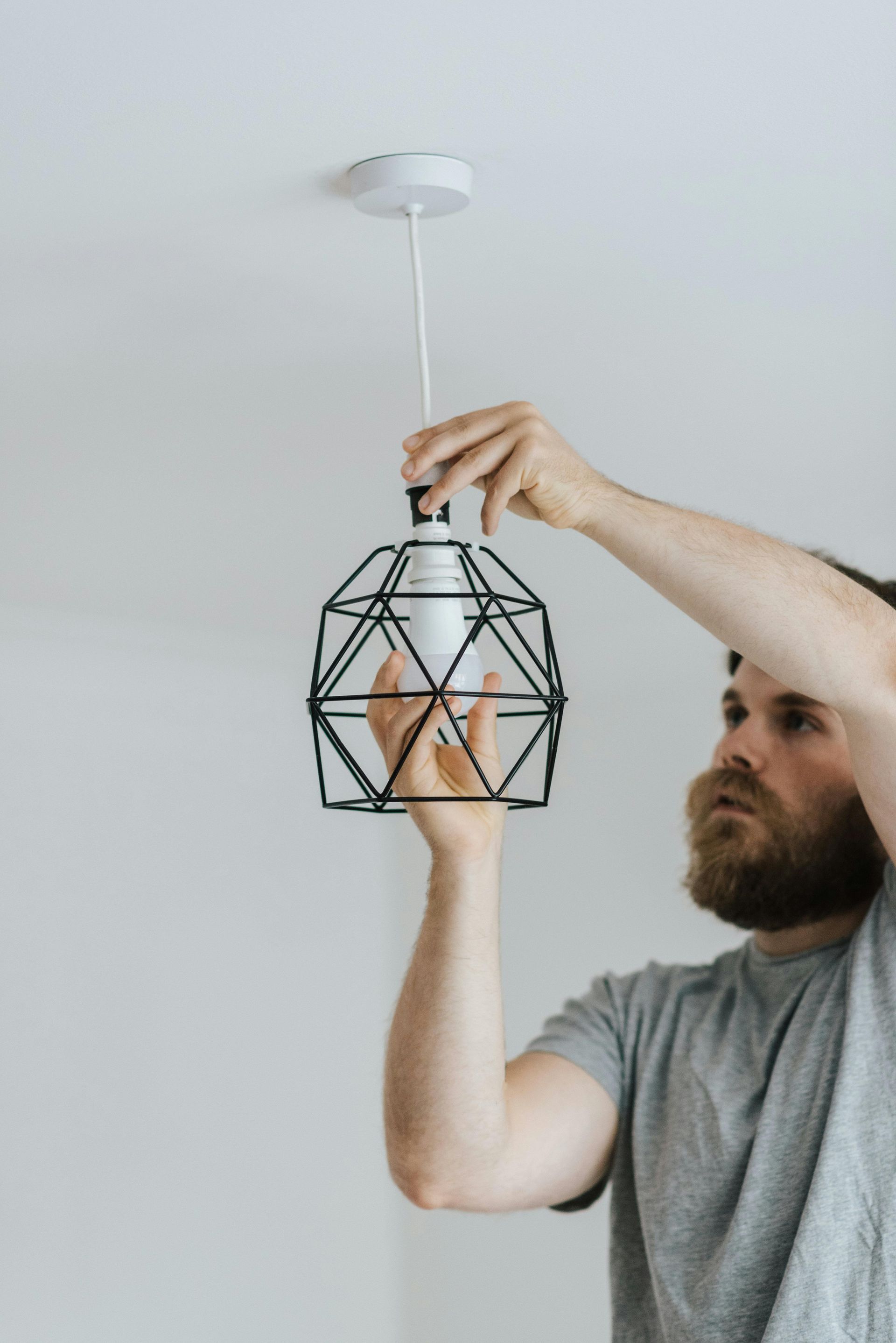 Man installing a geometric pendant light fixture on a white ceiling.