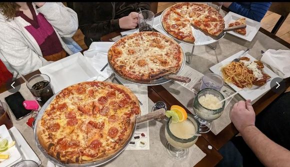 Shared table with several cheese pizzas, drinks, and folded napkins in a casual dining setting