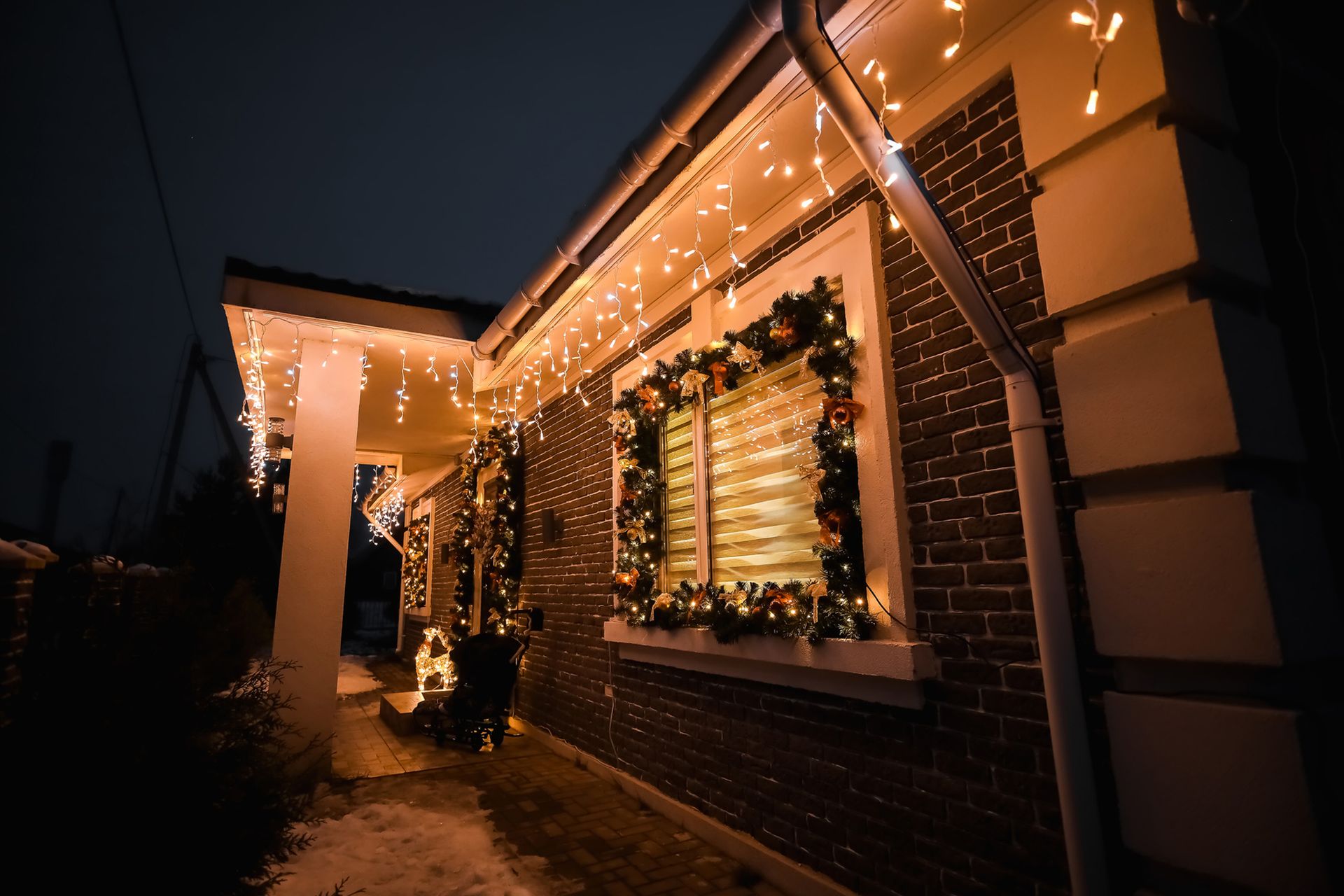 A brick house exterior at night, decorated with festive Christmas lights and a garland around the window.