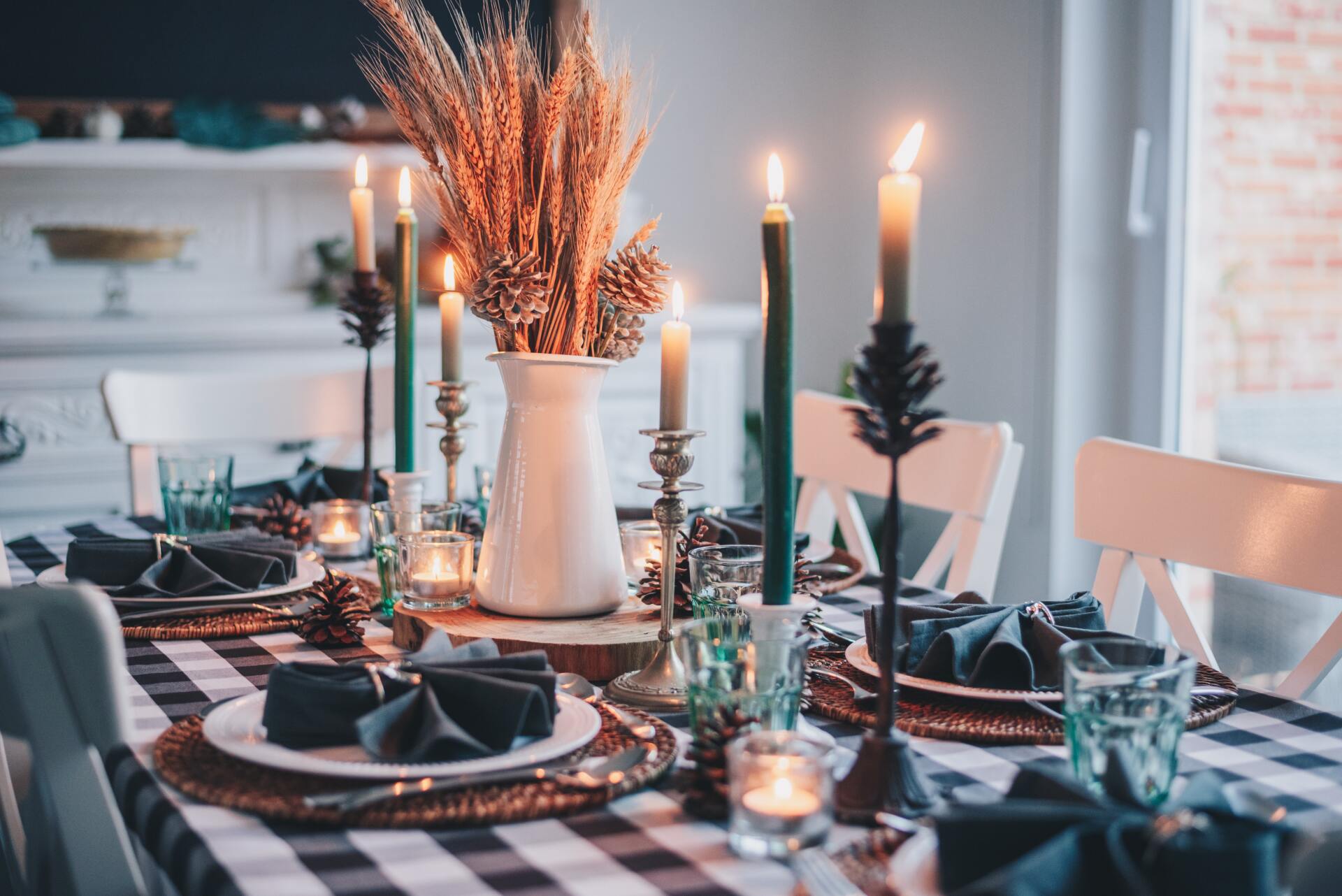 Table set up with checker table cloth, plates, napkins, candles, and a white vase with dried wheat and pinecones