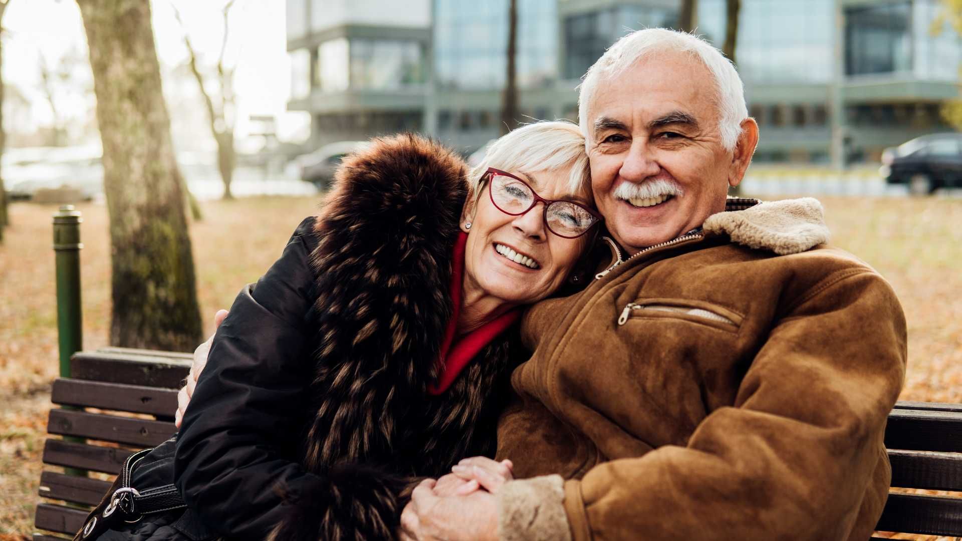 An elderly couple is sitting on a park bench.