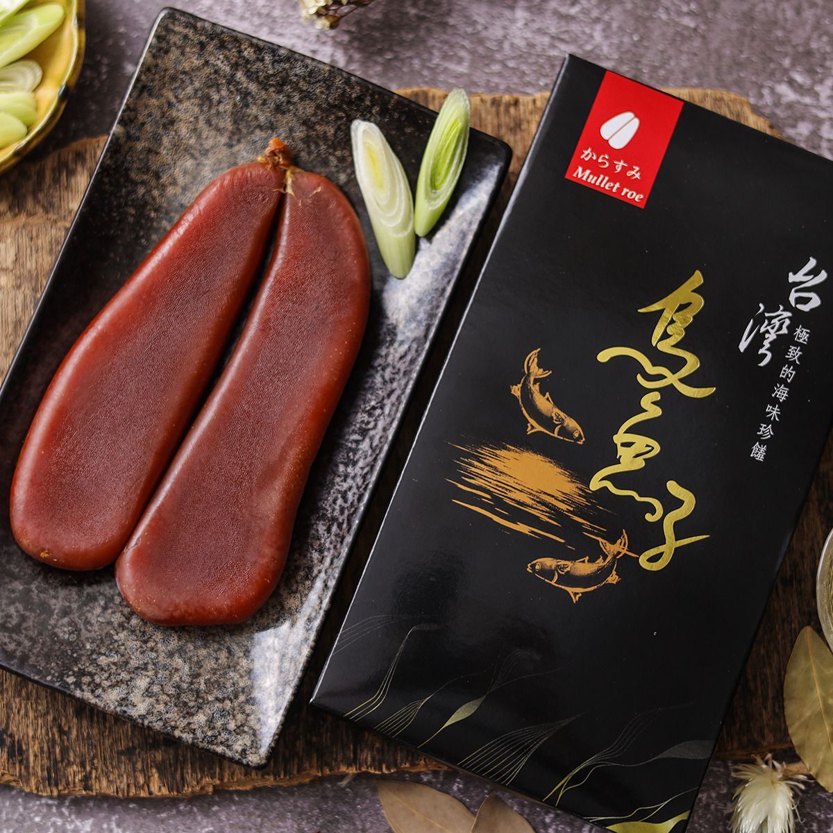 盤子裡放著兩顆乾枯的紅棕色鯔魚子，旁邊是一個印有金色漢字的黑色盒子。