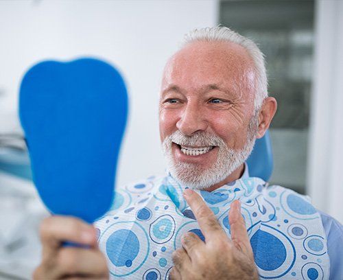 An older man is smiling while looking at his teeth in a mirror.