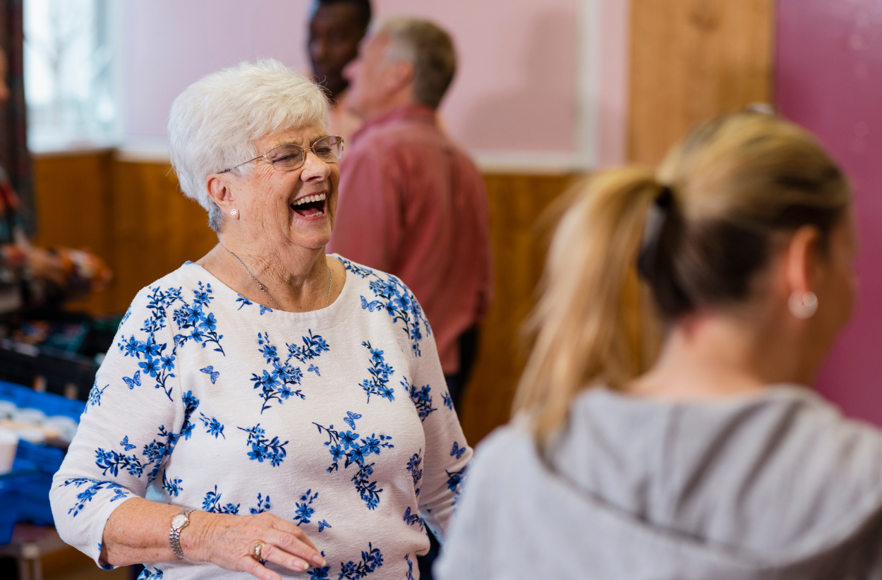 Smiling woman in floral shirt laughs with others in a room.