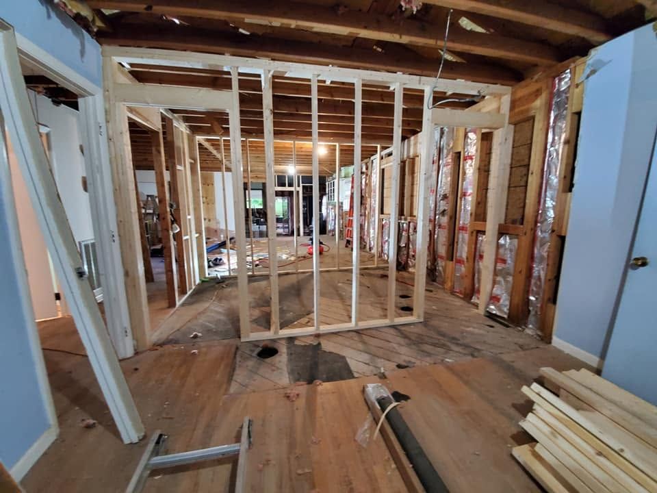Interior framing of a house under renovation, with exposed wooden studs, beams, and unfinished floors.