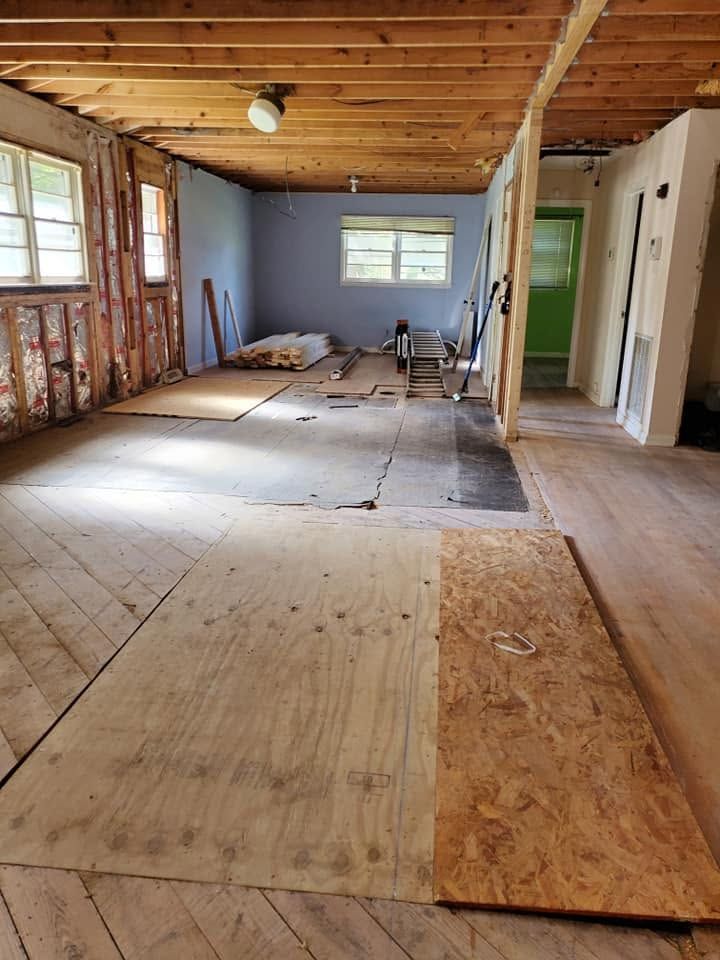 Renovation in progress in a bare room with exposed insulation, plywood flooring, and tools scattered inside.