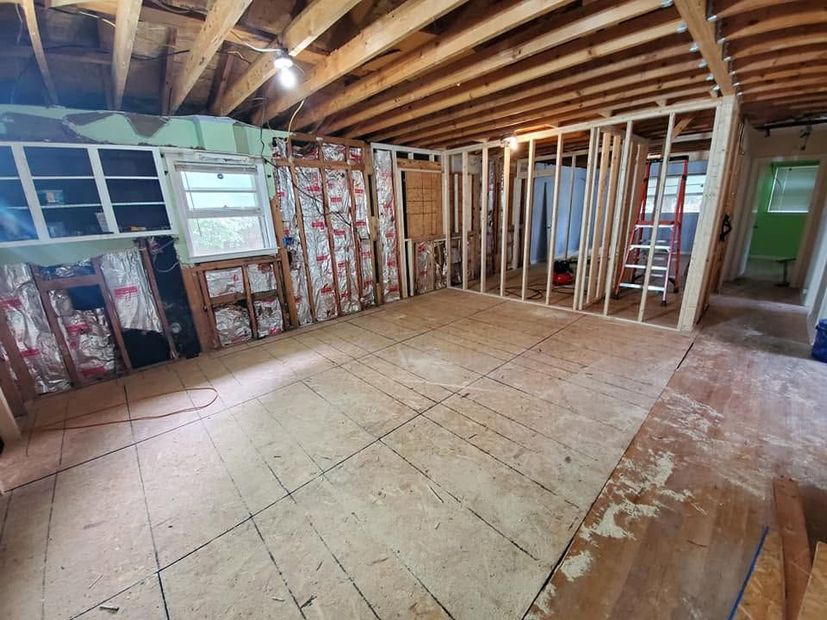 Interior of a house under renovation with exposed framing, unfinished floors, and ceiling beams