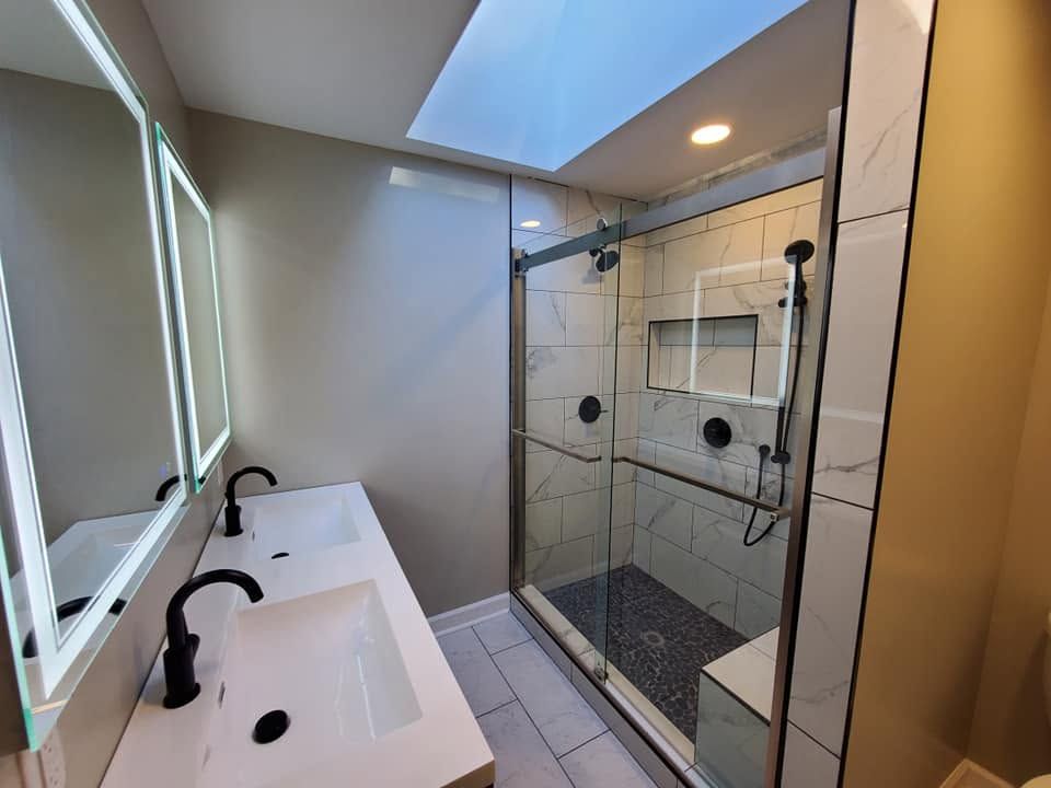 Modern bathroom with double sinks, lit mirror, and glass-enclosed shower.