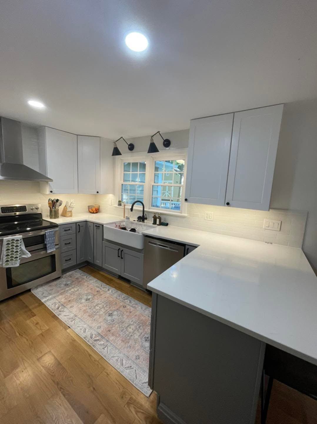 Bright modern kitchen with gray cabinets, white counters, stainless stove, and a patterned rug