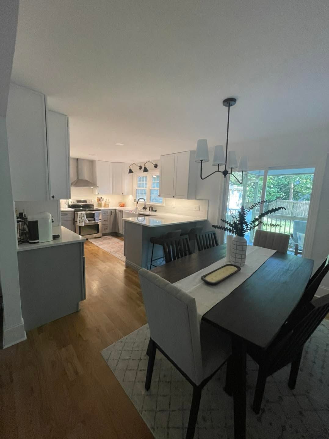 Open-plan dining and kitchen area with a dark table, white cabinets, and large windows.