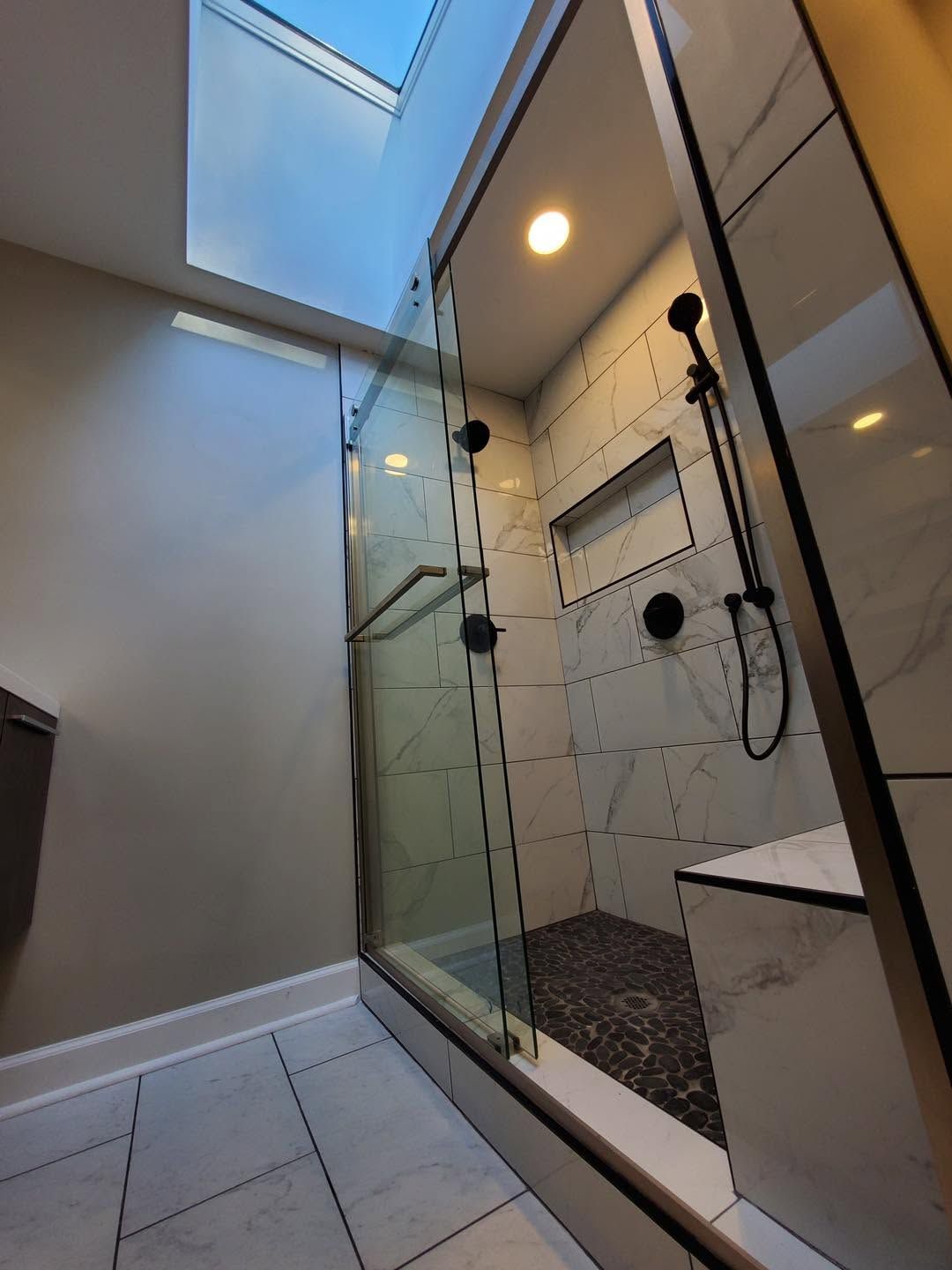 Modern bathroom shower with glass enclosure, tiled walls, skylight, and white vanity cabinet