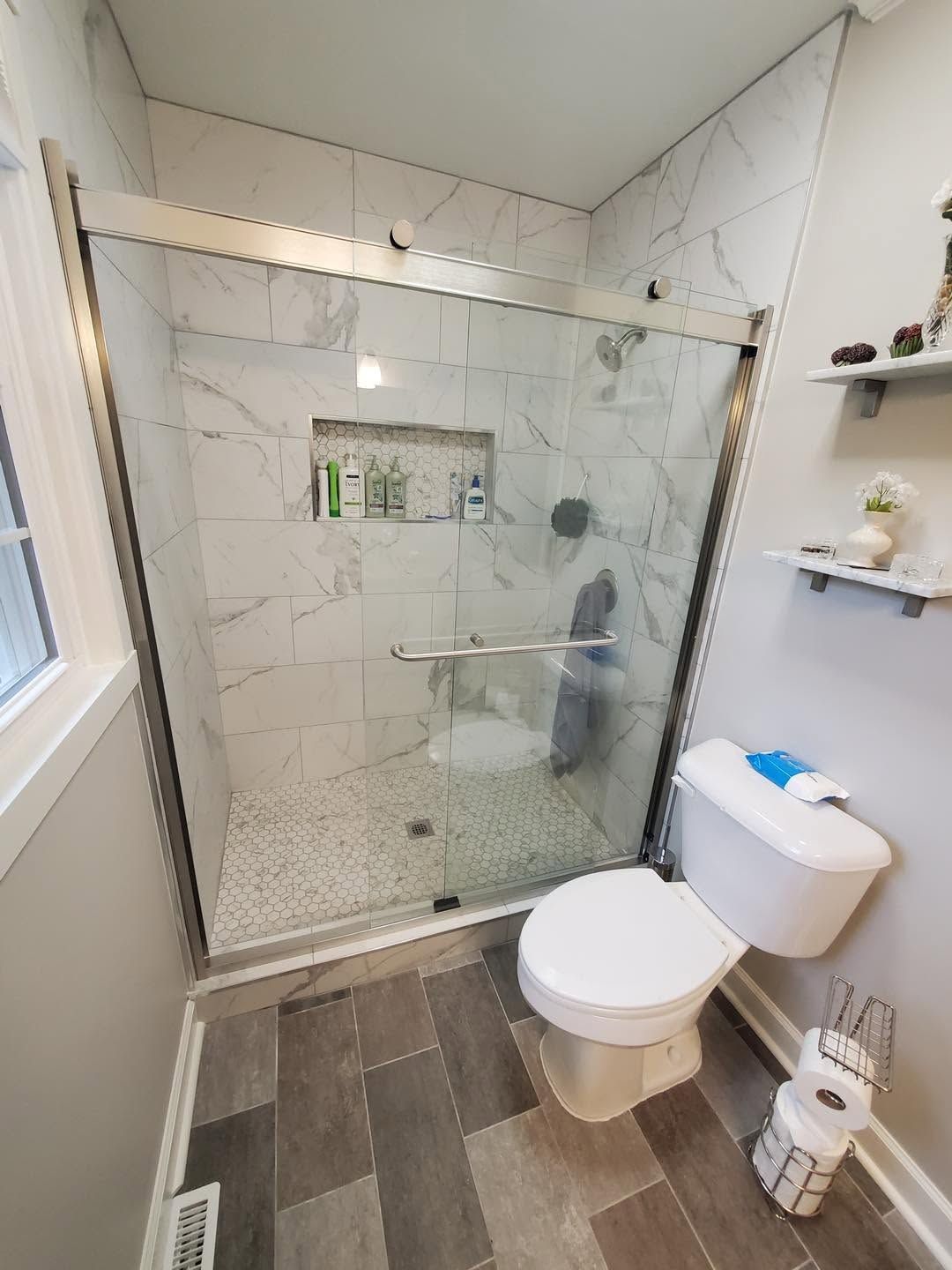 Small modern bathroom with glass shower, white tile, toilet, sink, and toilet paper holder.