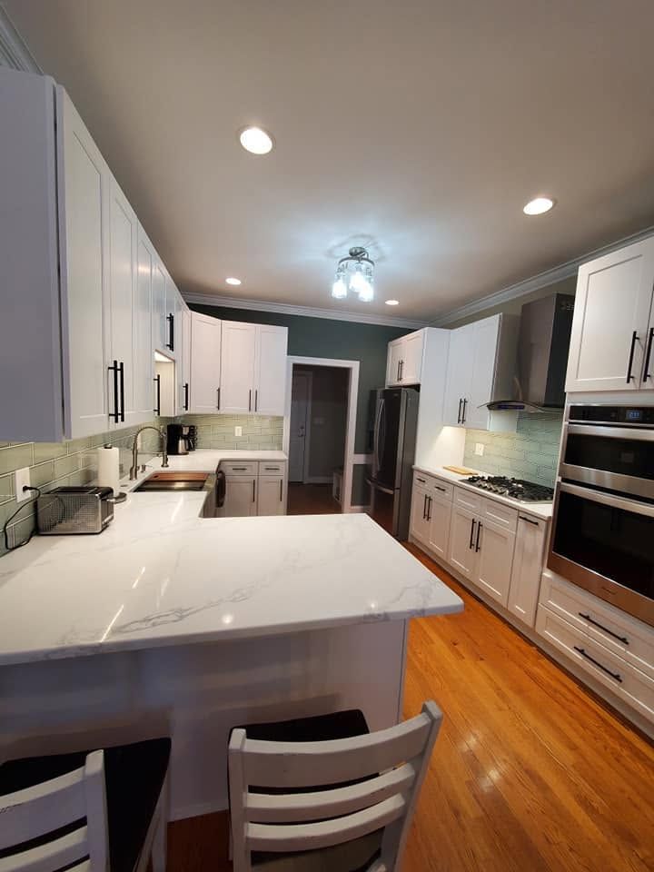 Bright white modern kitchen with island, stainless appliances, wood floors, and recessed ceiling lights