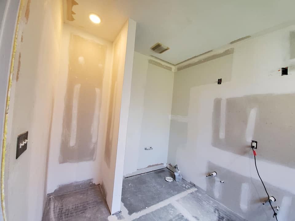 Small unfinished room with white walls, drywall patches, and exposed flooring under renovation