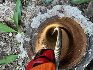 Red power drill with auger bit boring into a metal pipe opening in concrete ground