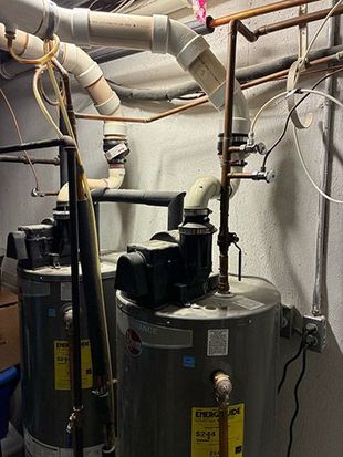 Basement utility room with water heaters, pipes, and ductwork.