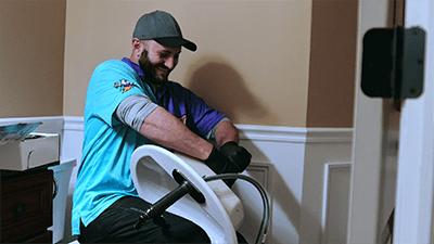 Man using a seated exercise machine indoors, wearing a teal shirt and black gloves.