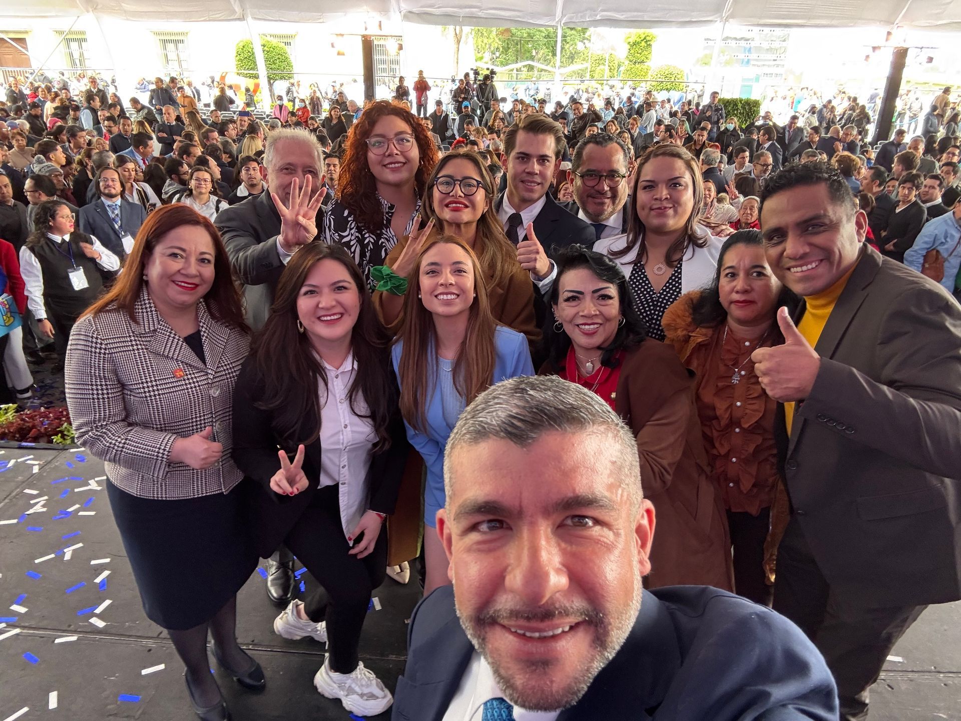 Group selfie at a crowded indoor event, with people posing and smiling in the foreground.