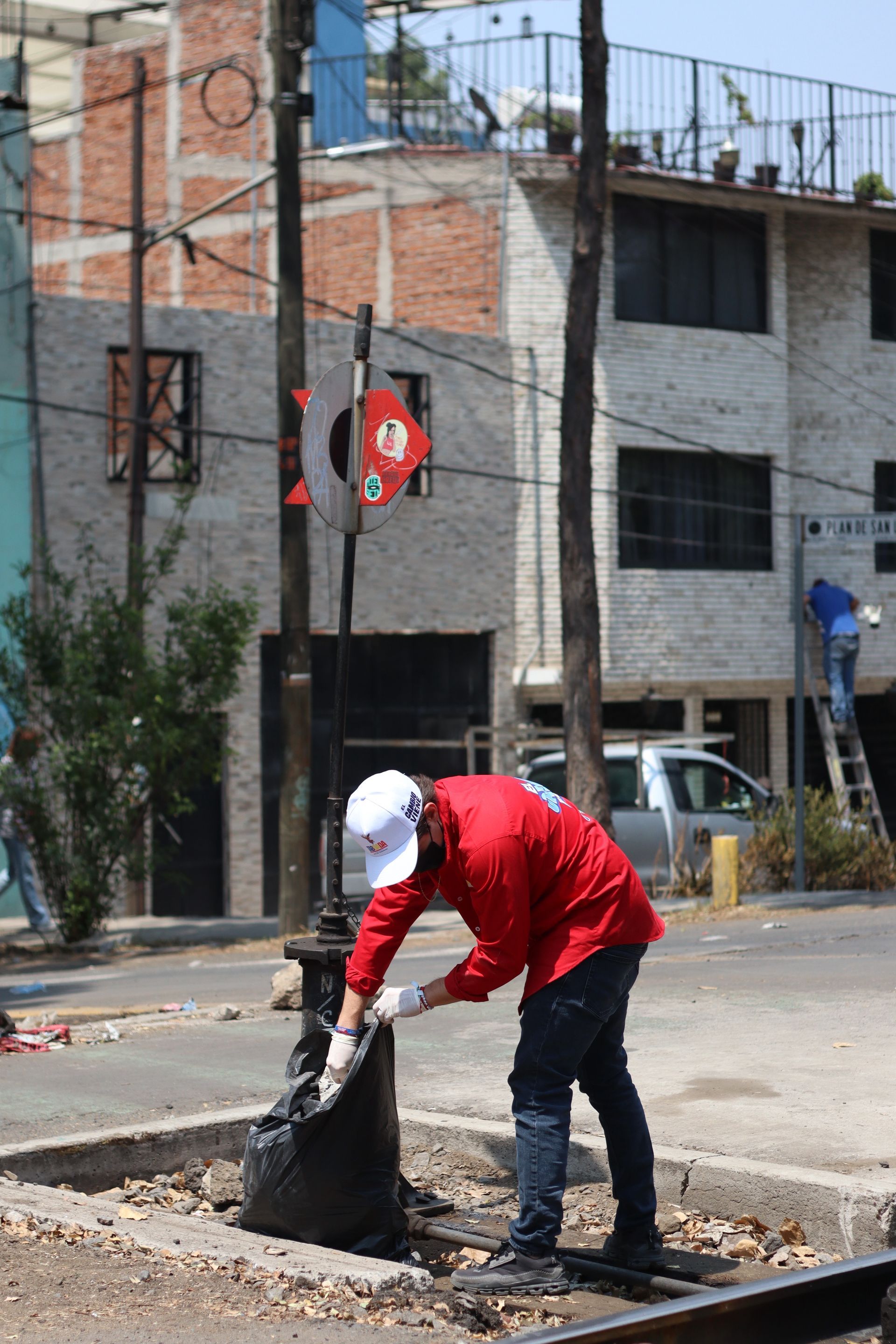 Worker in red shirt clearing debris from a street pothole in an urban neighborhood