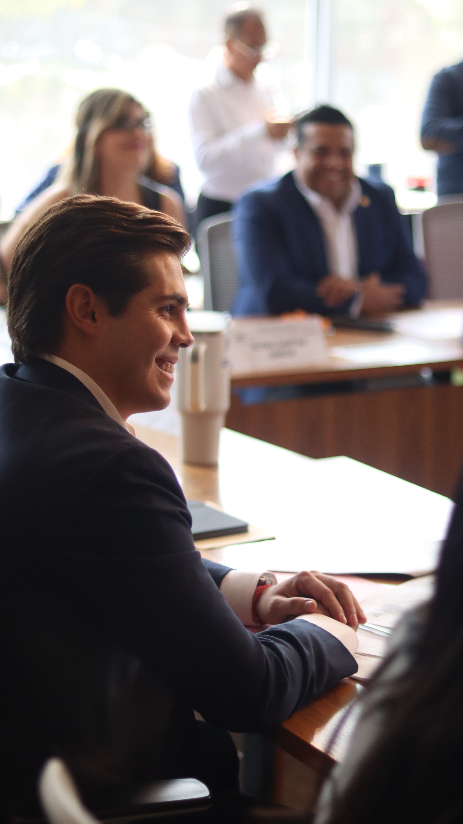 Business meeting in a conference room, with people seated at a table and one man in the foreground.
