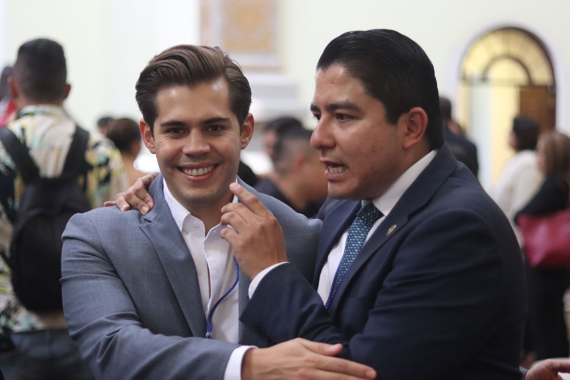 Two men in suits smiling and shaking hands at a formal indoor event