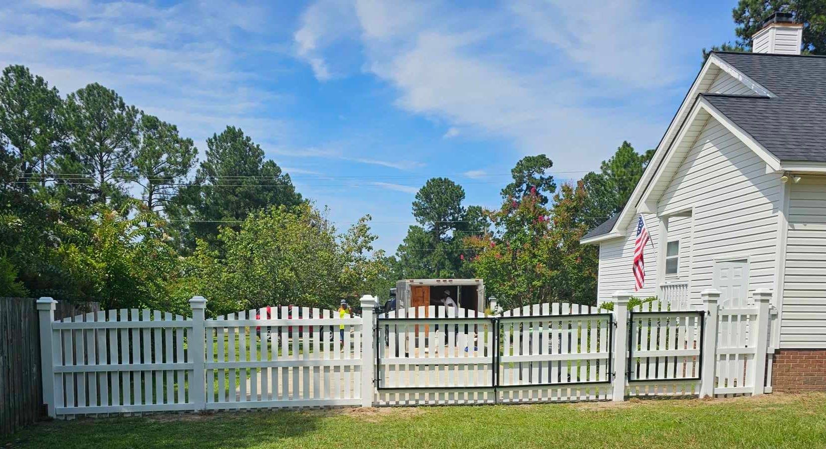 A white picket fence is in front of a white house.