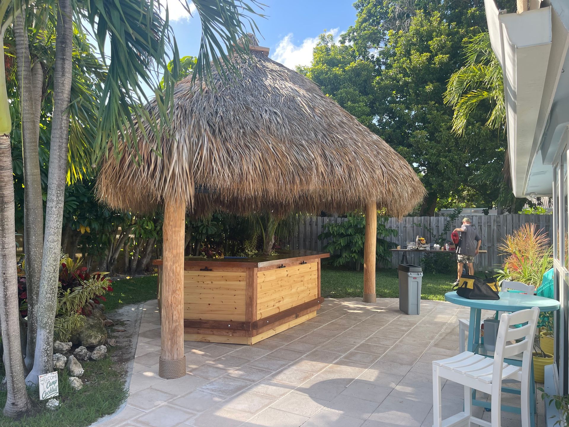 Thatched tiki hut bar on a sunny patio with palm trees and outdoor seating