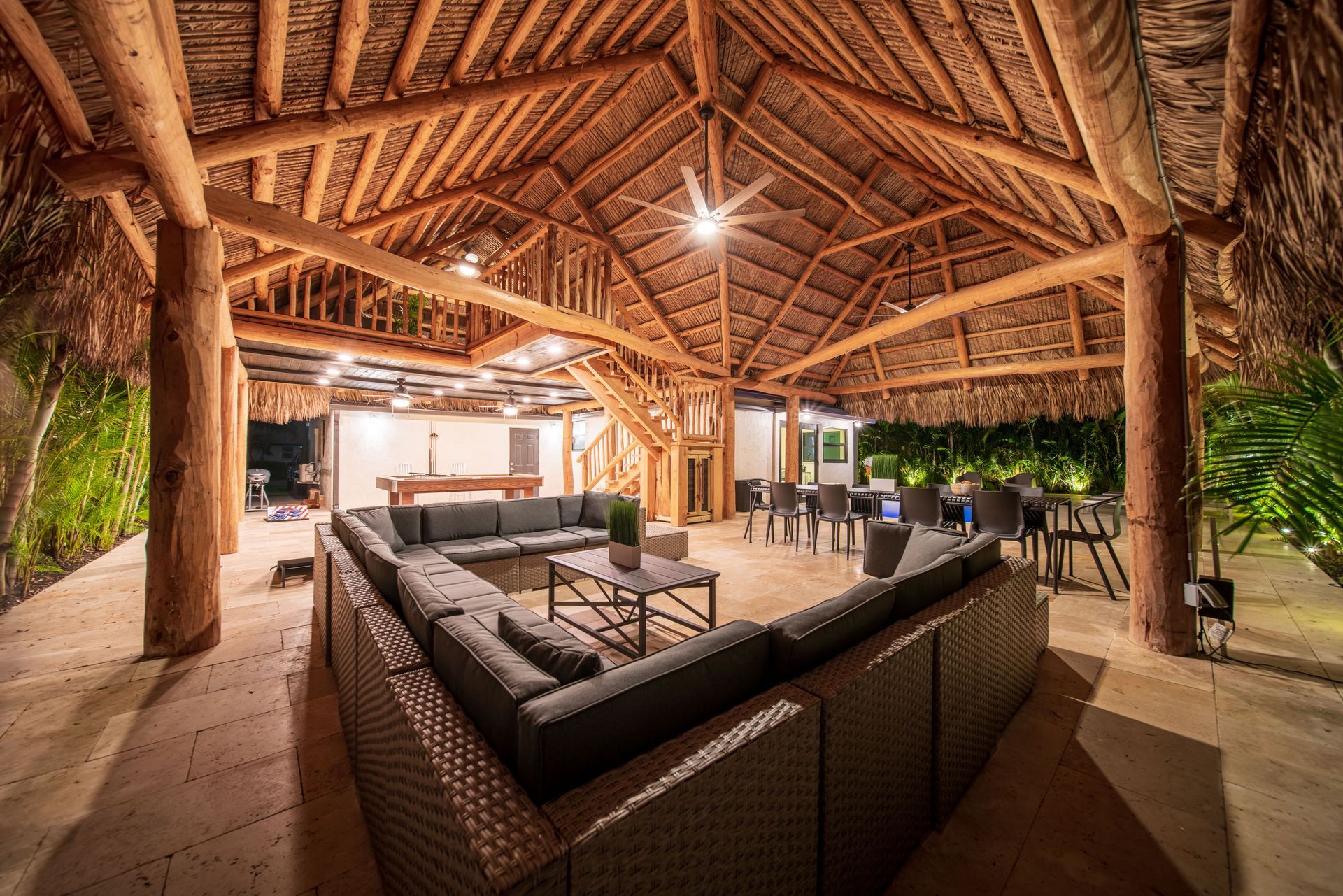 Open-air lounge with wicker sofas under a rustic thatched roof, lit warmly at night.