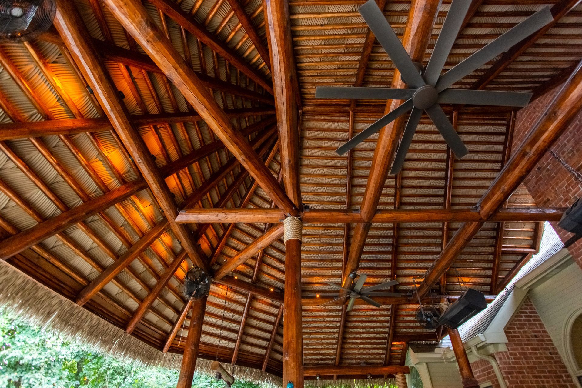 Wooden thatched roof with exposed beams and a ceiling fan in a rustic open-air structure