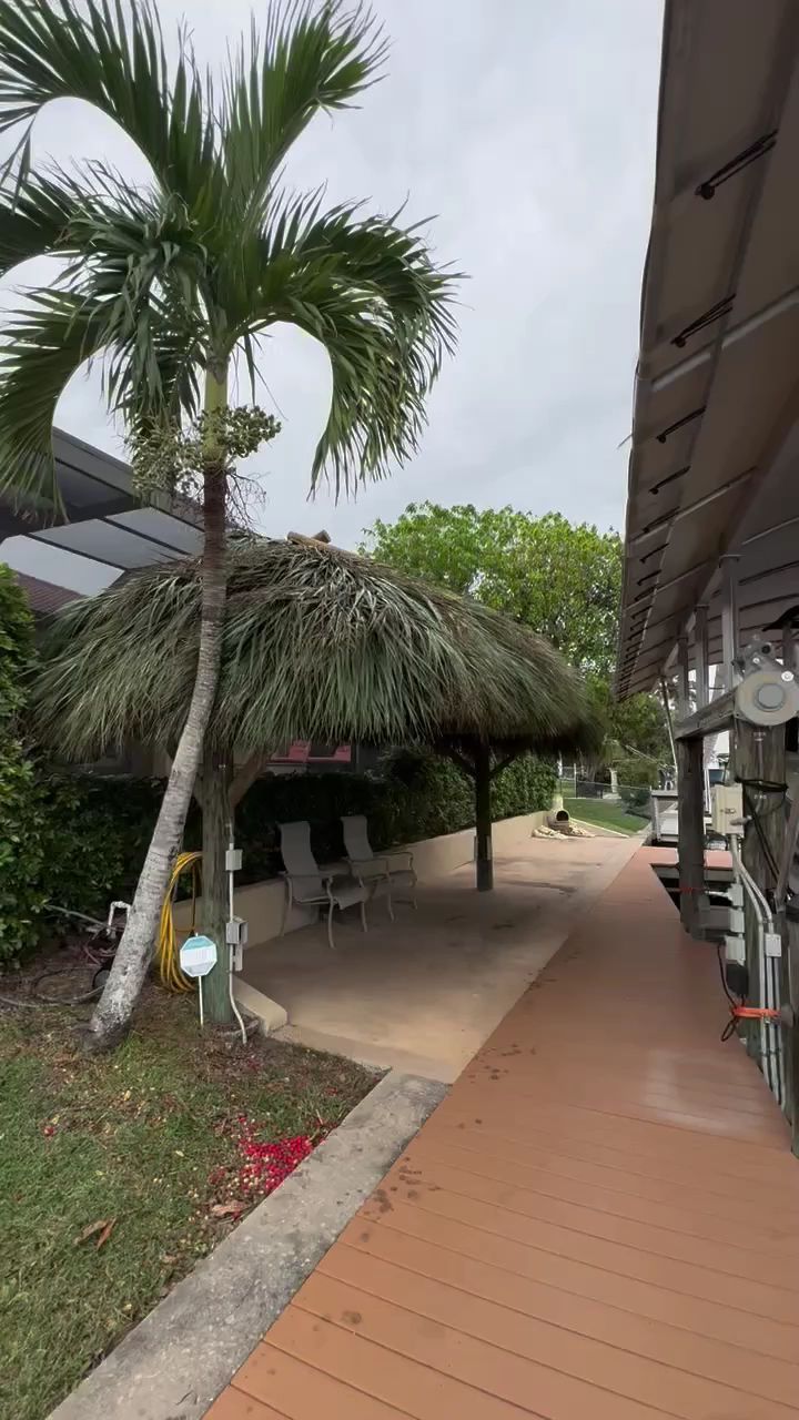 Tropical resort walkway with palm trees, thatched hut, and covered patio along a tiled path
