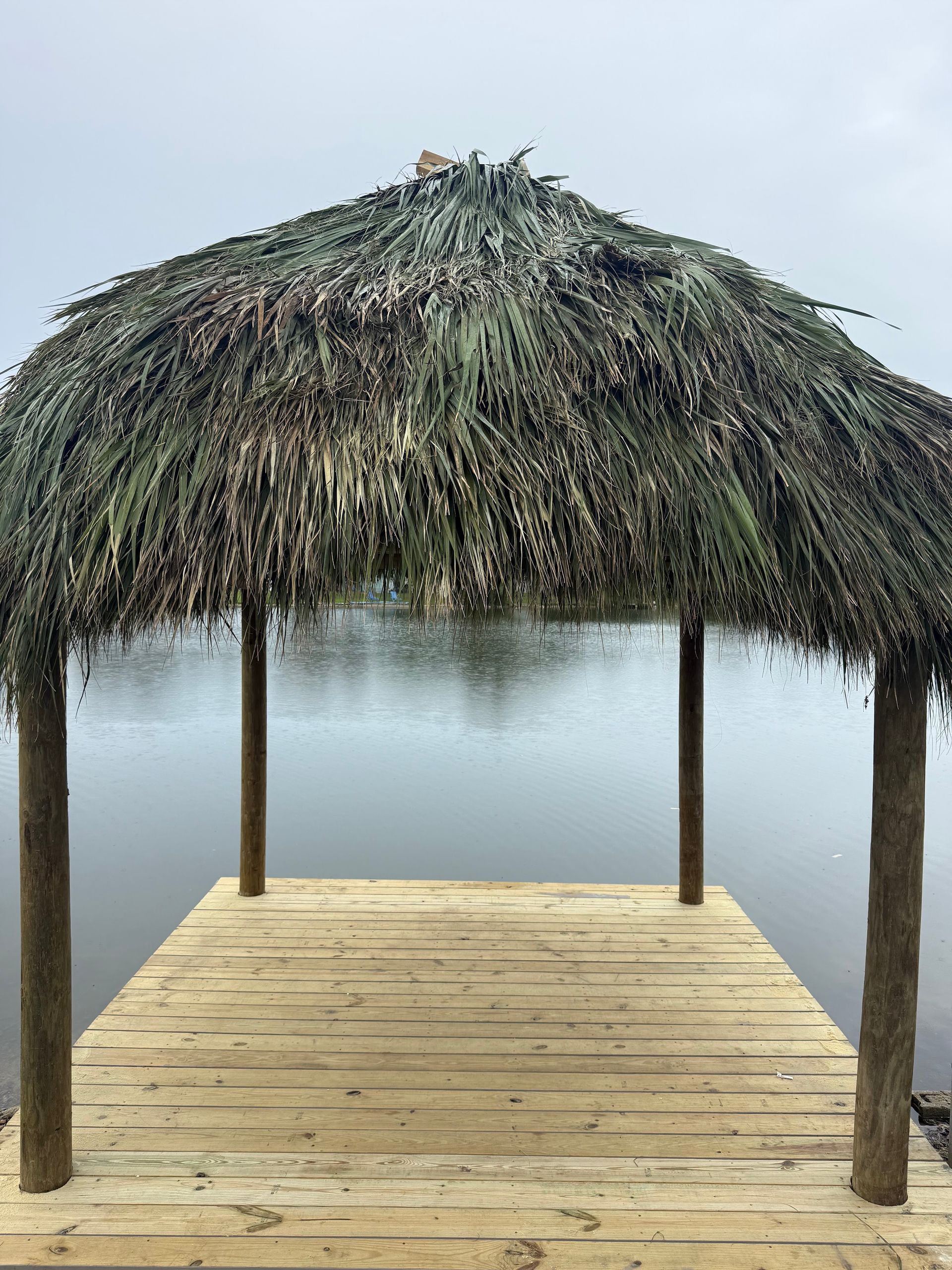 Thatched-roof pier over calm foggy water